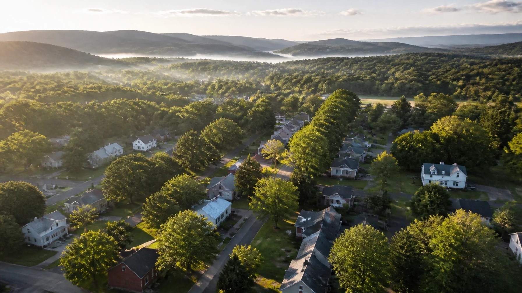 An aerial view of a residential neighborhood surrounded by trees and rolling hills, showcasing a growing suburban community.
