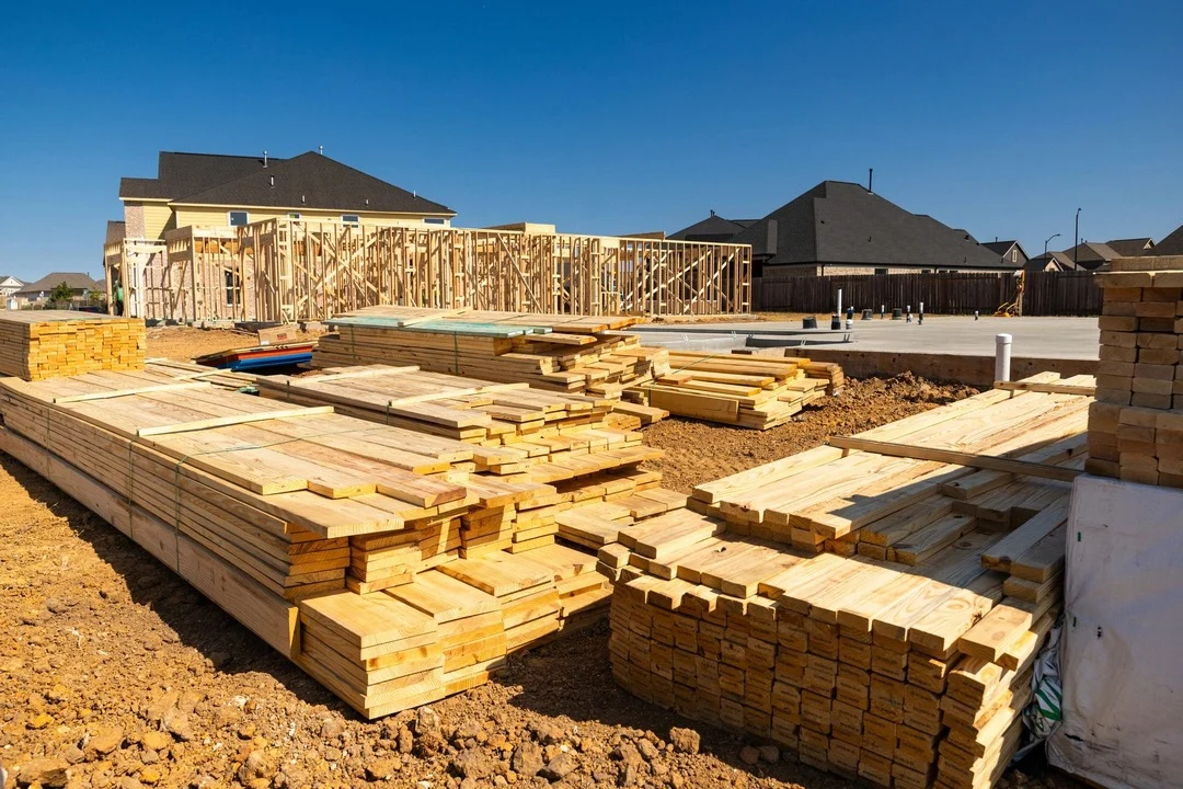 A home being constructed, currently only displaying the laid foundation, some framing and stacks of wood.